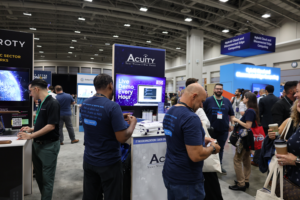 People in Acuity-branded shirts at the Acuity booth at AWS Summit. The computer demonstrating the GenAI Chatbot is visible. 