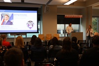 Image of people in a conference room, with a man (conference speaker David Larrimore) at the podium being introduced by a woman (Laura MacDonald).